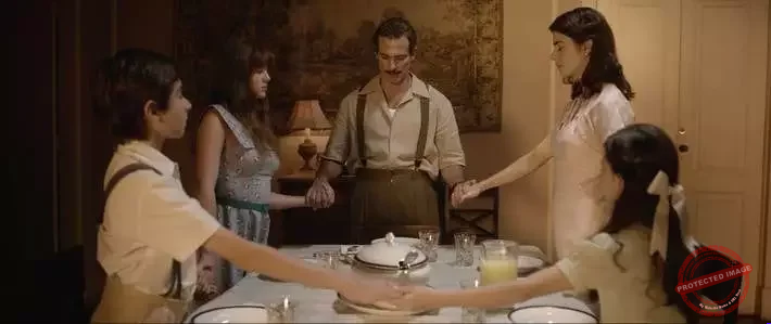 Família de três gerações conversando com carinho na sala, com uma senhora segurando a mão de um jovem